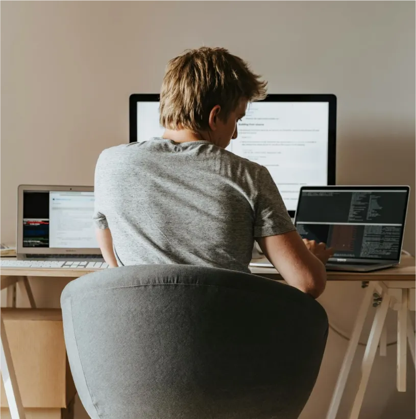A programmer working at a desk with 2 laptops and a monitor.